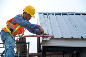 Roofer with electric drill used on new roofs with Metal Sheet on top roof at the building under...