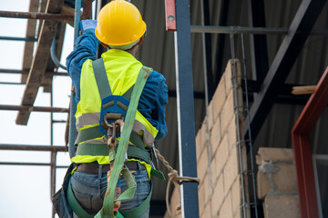 Construction worker wearing safety harness and safety line working at the building under...