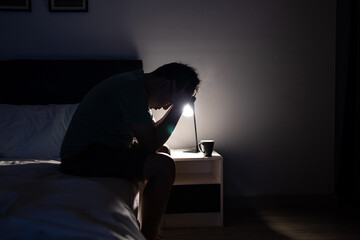 Depressed asian man crying covering face with his hands,sitting on the bed at night,Stressed...