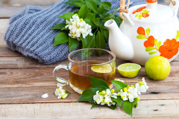 Obraz na płótnie Canvas herbal healthy drinks hot lemon tea health care for cough sore with lemon slice ,jasmine flowers and knitting wool scarf of lifestyle woman relax winter arrangement flat lay style on background wooden