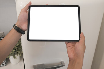 Mock up image of hand holding digital tablet with white screen in kitchen.