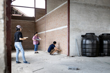 Asian family visiting their new home being built,inspect the house structure,man measuring size of the room on the brick walls,building improvement,plan to expand,renovation and construction concept