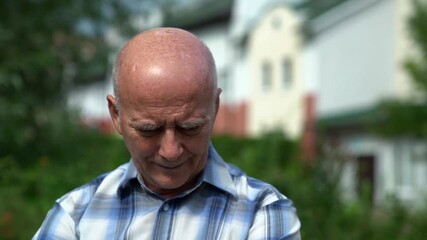 elderly bald man is sitting and resting outdoors at summer day