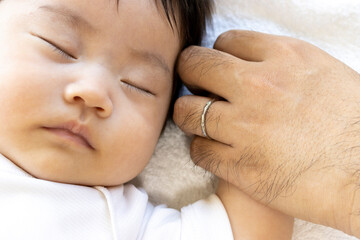 Fototapeta na wymiar 寝ている赤ちゃんと、赤ちゃんの手を握る男性の手