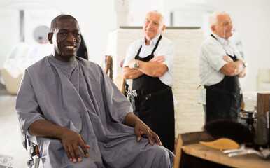 African-American man approving result of hairdresser work, looking satisfied with his new hairdo