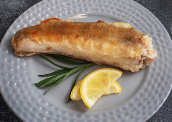 Fried fish hake Pollock and slices of fresh lemon. Dark concrete background. Copy space.