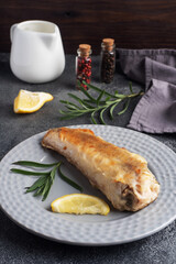 Fried fish hake Pollock and slices of fresh lemon. Dark concrete background. Copy space.