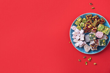Middle Eastern sweets. Turkish delight with pistachios nuts on plate over red background. Top view. Copy space. Arab dessert, rahat lokum, sherbet, nougat, churchkhela, cookies. Flat lay.