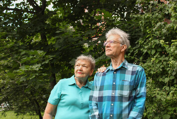 Happy elderly couple stands against a background of green foliage in the park. International Day of Older Persons and Grandparents Day
