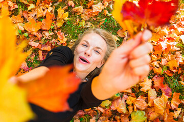 Naklejka na ściany i meble Woman lying on the grass with fallen orange leaves