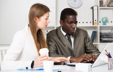 Male and female colleagues working with laptop and documents at table in office