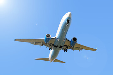 Fototapeta na wymiar modern airplane flying high against blue sky background. Passenger plane landing. Jet aircraft in air with gear and flaps extended. Belly view of business jet. Aviation wallpaper