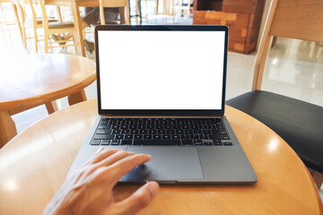 Mockup image of a hand touching on laptop computer touchpad with blank white desktop screen on wooden table