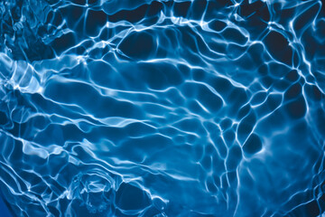 De-focused transparent dark blue colored clear calm water surface texture with splashes and bubbles. Trendy abstract nature background. Water waves in sunlight with copy space.