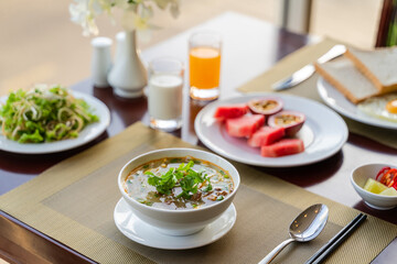 Fresh romantic breakfast table next to window with bread, fruit, juice, milk, noodle soup