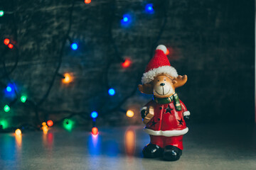 deer dressed as santa claus on the background of a dark wall with a christmas garland