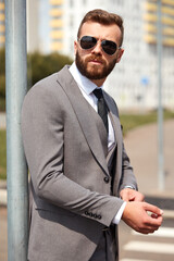 stylish successful businessman in suit and in sunglasses fix a tbutton outdoors.