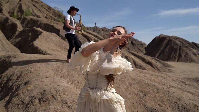 dancing woman and male saxophonist in desert with rocks, two musicians at nature