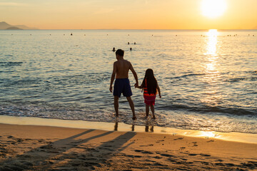 Father and daughter walking on the beach in the dawn time