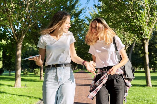 Two beautiful happy girls teenagers 17, 18 years old walking together in park