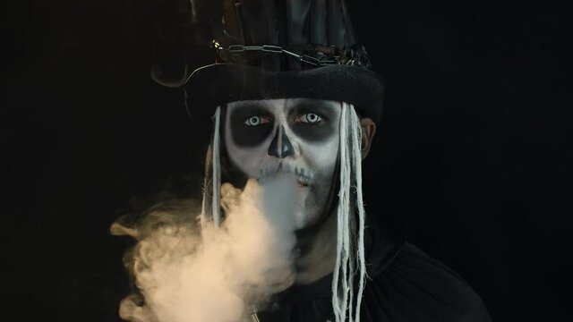 Frightening man in creepy skeleton Halloween cosplay exhaling cigarette smoke from his mouth