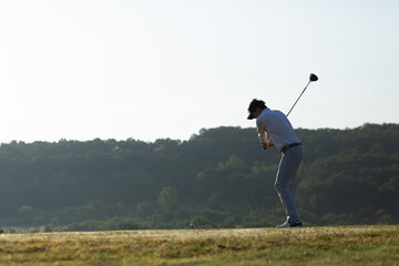 Golfer plays swing shot on teeing ground in warm sunshine. View from the side. leisure and sport concept.