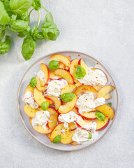 Delicious summer salad with peaches, Strachatella cheese, honey, olive oil and fresh Basil. Selective focus, top view.