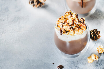 Cold winter chocolate dessert with whipped cream, popcorn and caramel topping in glasses on beige background, place for text