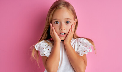 portrait of little caucasian girl in shock, she is surprised by something, hold hands on cheek,...