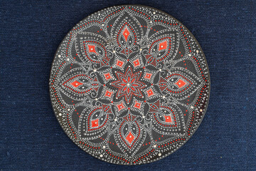 Decorative ceramic plate with red and silver colors, painted plate on background of blue fabric, dot painting
