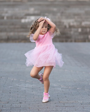 Little Girl In Pink Dress Spinning Around On The Street