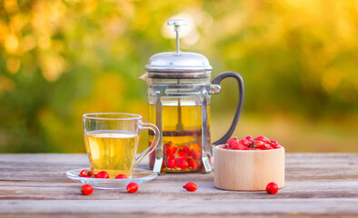 A teacup of hot rosehip tea on a wooden table in the autumn garden.