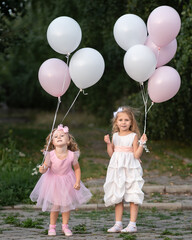 Little girls in pink and white dressses with balloons walking in the park