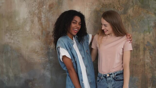 Black girl and caucasian young woman hug each other with affection. Two loving friends laugh together. Medium shot.