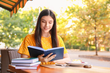 Beautiful young woman reading book in street cafe