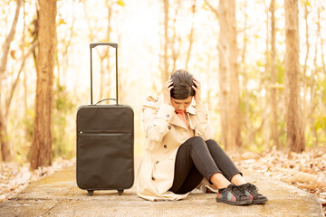 スーツケースの横に座り頭を抱える女性