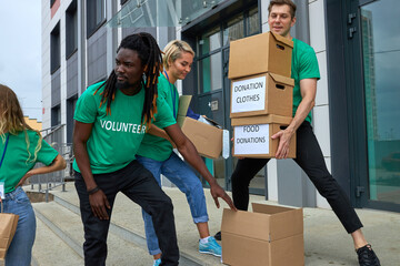 friendly interracial charity group engaged in voluntary, they stand outdoors on stairs transfering...