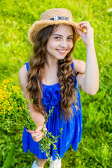 Natural beauty. Happy child hold flowers natural landscape. Little girl smile with sun hat on long wavy hair. Summer fashion and accessory. Beauty and spa salon. Skincare and haircare