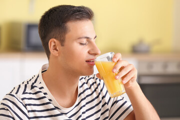 Fototapeta premium Handsome man drinking fresh orange juice in kitchen