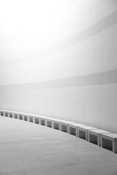 Black and white vertical image of row of marble seats along a tall building wall