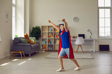 Excited boy in superhero cape and helmet playing at home. Child dressed as comic character having fun indoors