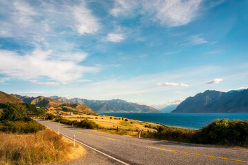 Picturesque perspective view of Highway 6 on the side of Lake Hawea with mountain peaks in the distance in Otago Region, New Zealand, Southern Alps.