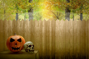 Jack-o-Lantern and human skull on the table with a wooden fence