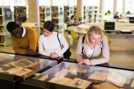 Professor and adult students read ancient books in a library showcase. High quality photo