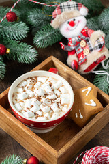 Cocoa with marshmallows in a red Cup and gingerbread on a tray on a Christmas background. Red decorations on spruce branches on a brown background