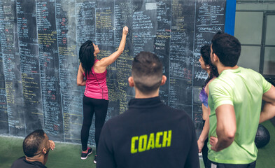 Athlete woman writing down results on the gym blackboard with her classmates and coach