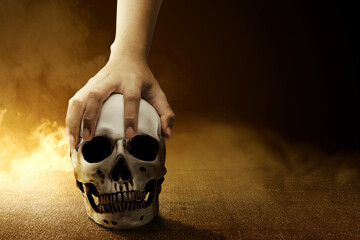 Hand holding a human skull on the concrete floor with smoke
