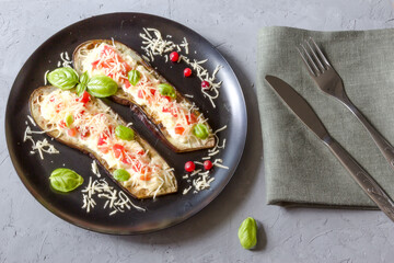 Fried eggplant stuffed with tomatoes, grated cheese, yogurt dressing and cranberries, garnished with Basil leaves on a dark plate over gray slate, stone or concrete.Top view.