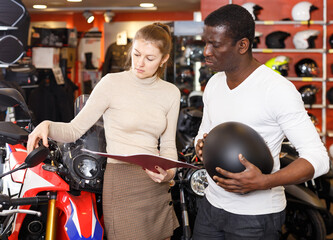 Confident female seller helping man to choose new motorcycle and riding gear in salon