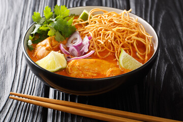 Khao Soi is a creamy, slightly spicy yellow curry noodle dish found in Northern Thailand closeup in the bowl on the table. Horizontal